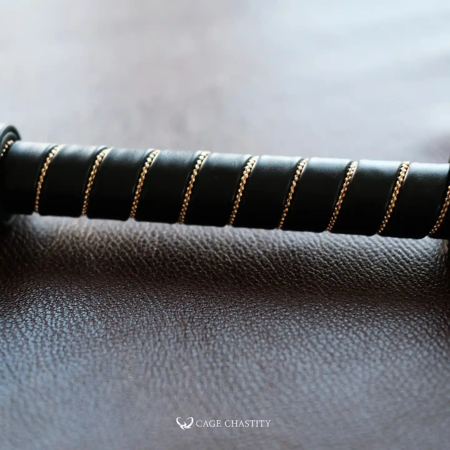 the handle details of the flogger whip, black leather with gold stitching