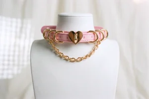 white mannequin wearing a pink sissy collar with gold hardware